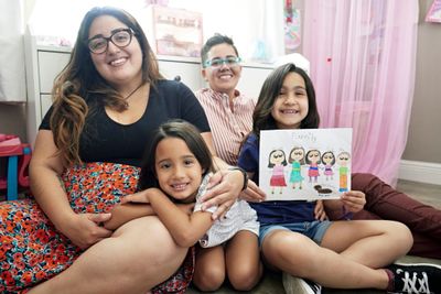A happy family of four sitting together, with a child holding a family drawing.