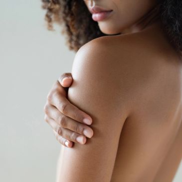 Close-up of a woman holding her bare shoulder.