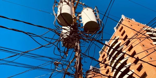 Tangled electrical wires around a utility pole near a building under clear blue sky.
