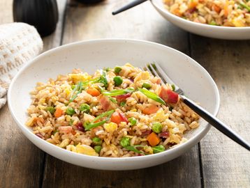 A bowl of colorful fried rice with peas, carrots, eggs, and green onions.