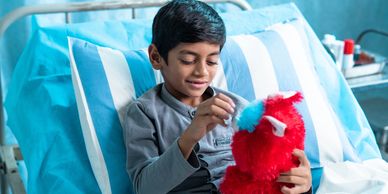 A boy in a hospital bed playing with a red stuffed toy.