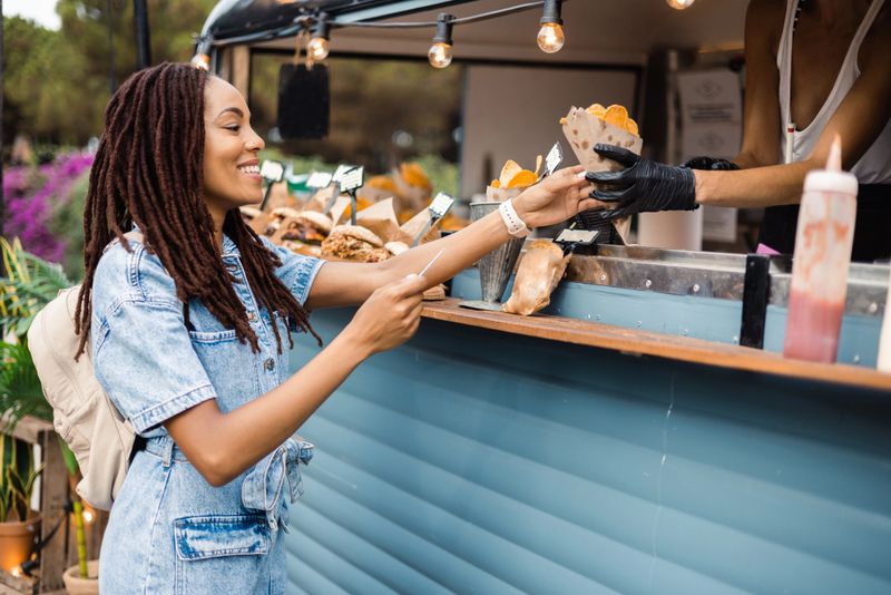 Beautiful African American young woman buying fast food at the food truck on the street