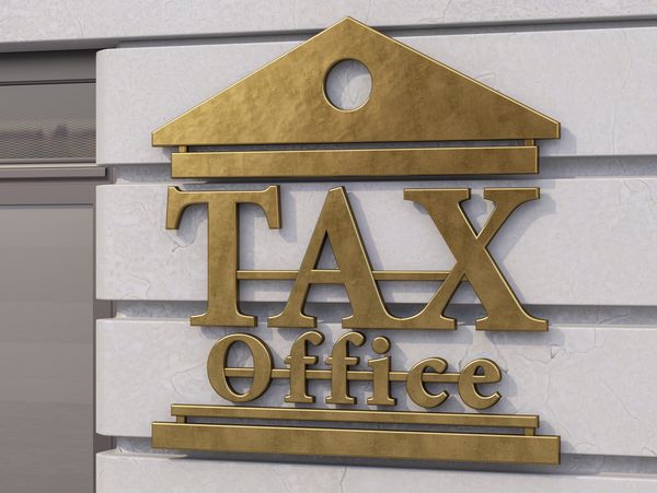 Gold sign reading 'TAX Office' mounted on a marble wall.