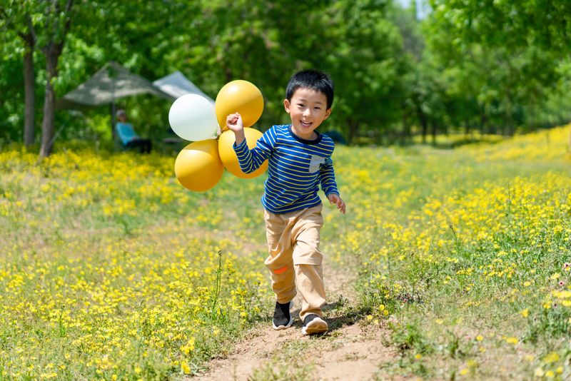 A joyful child playing with colorful balloons in a sunny park, captured in a candid moment.