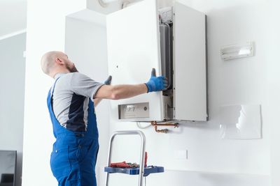 Technician installing or repairing a wall-mounted boiler in a clean, modern room.