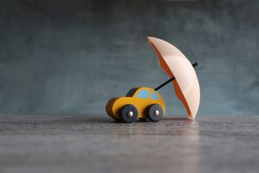 A small yellow toy car under a white umbrella on a gray surface.