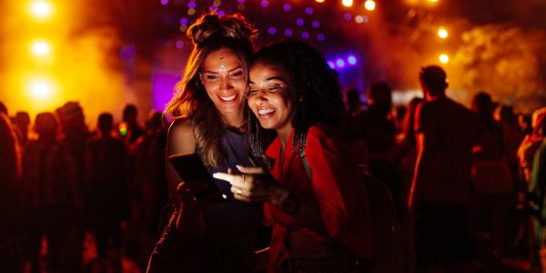 Two women enjoying music festival while looking at a phone.