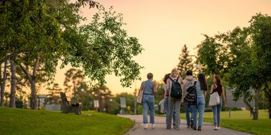 A group of five people walking on a park path during sunset.
