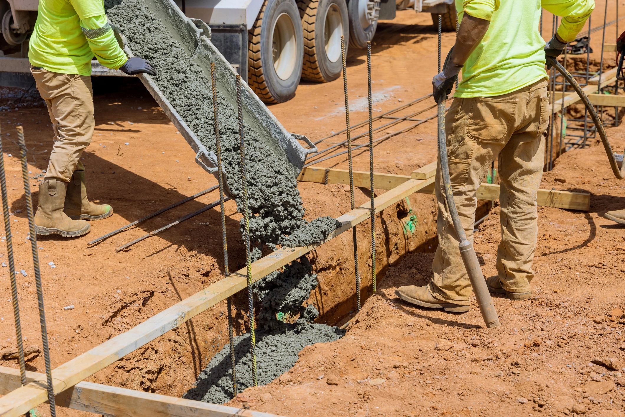 Construction workers pouring concrete into foundation trenches at a building site.