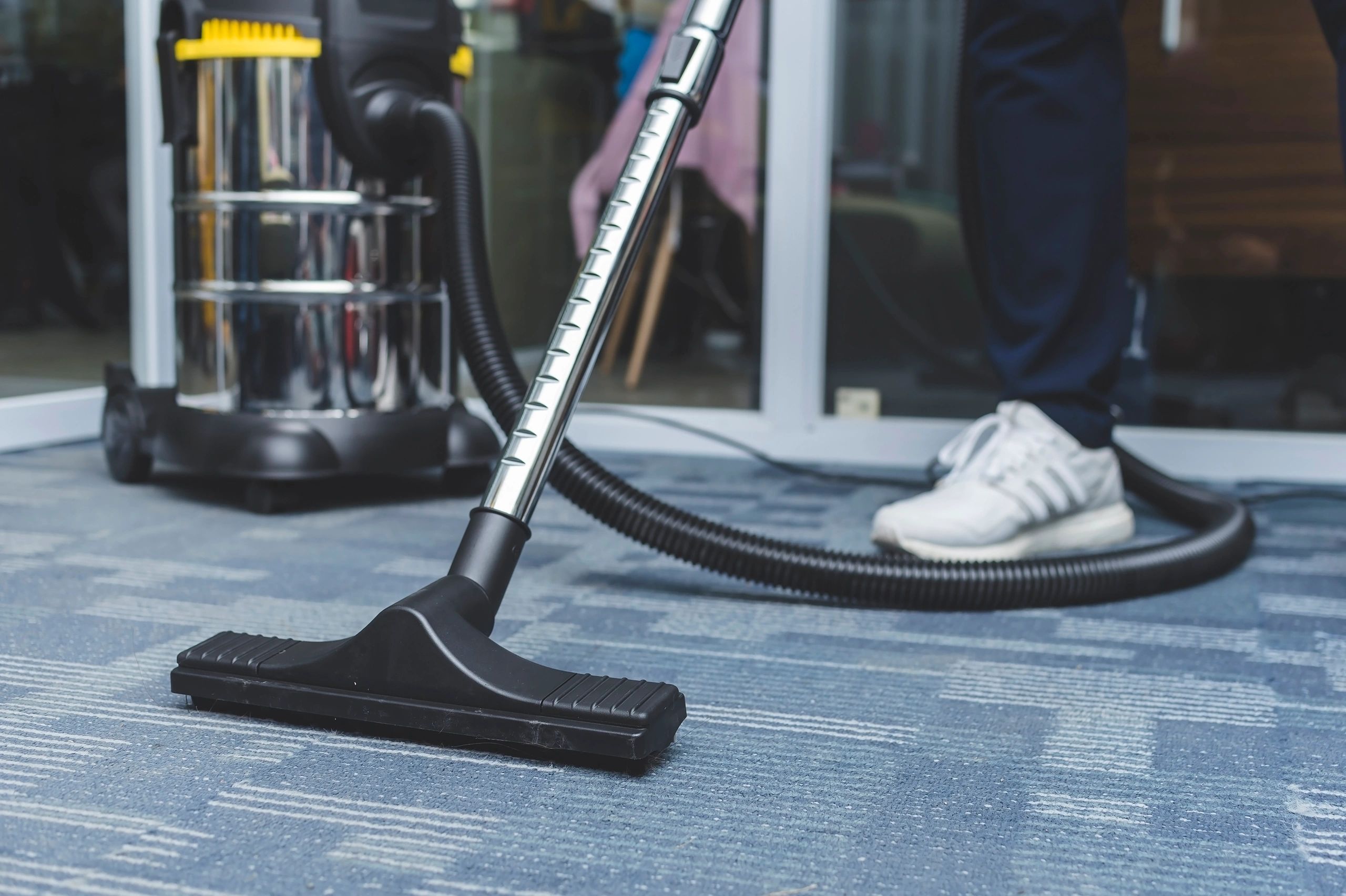 Vacuum cleaner on carpet with person wearing white sneakers.