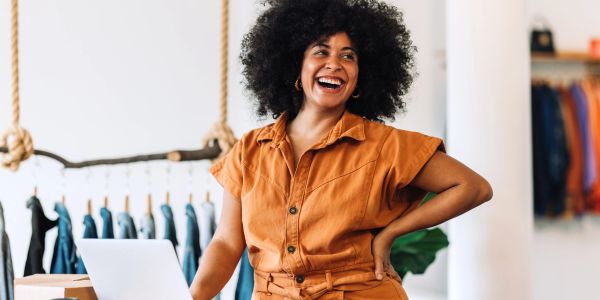 Happy woman standing with laptop in a clothing store.