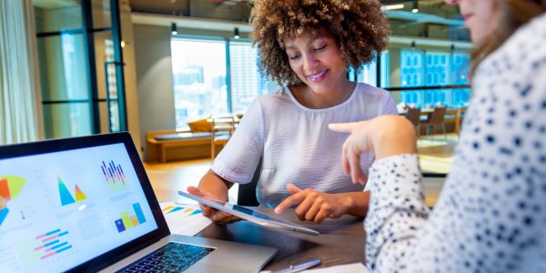 Two women collaborating in an office with charts and a laptop.