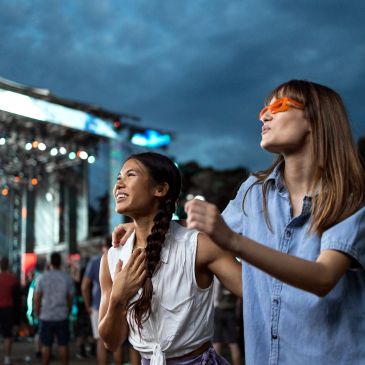 Two women enjoying a concert outdoors at dusk.