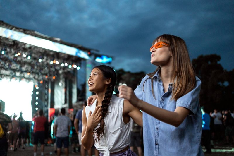 Two Asian and Caucasian girls dance in front of a stage and enjoy the atmosphere at a music festival.