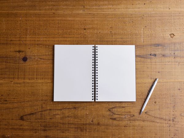 Open blank notebook with a pen on a wooden table.