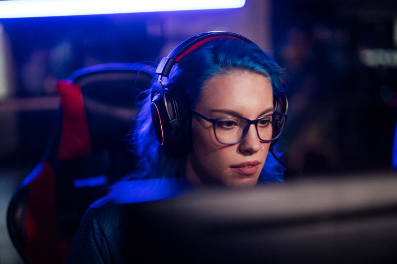 A blue-haired female with a headset participates in an esports tournament