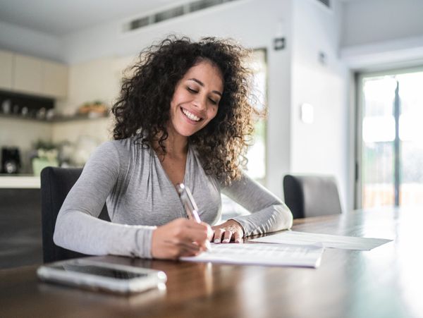 Happy woman signing documents at a table in a bright room.