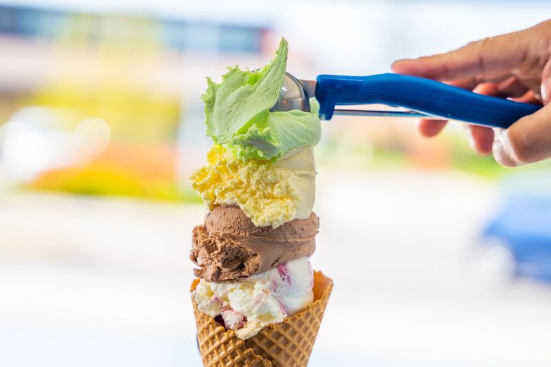 Male hand serving various flavors ice cream scoops in waffle cone