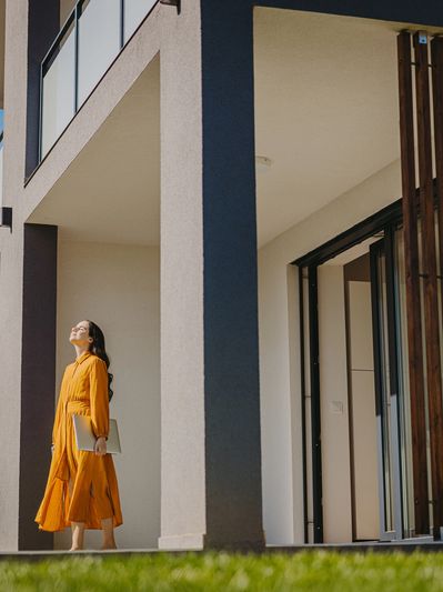 Woman in orange dress enjoying sunlight outside a modern building.