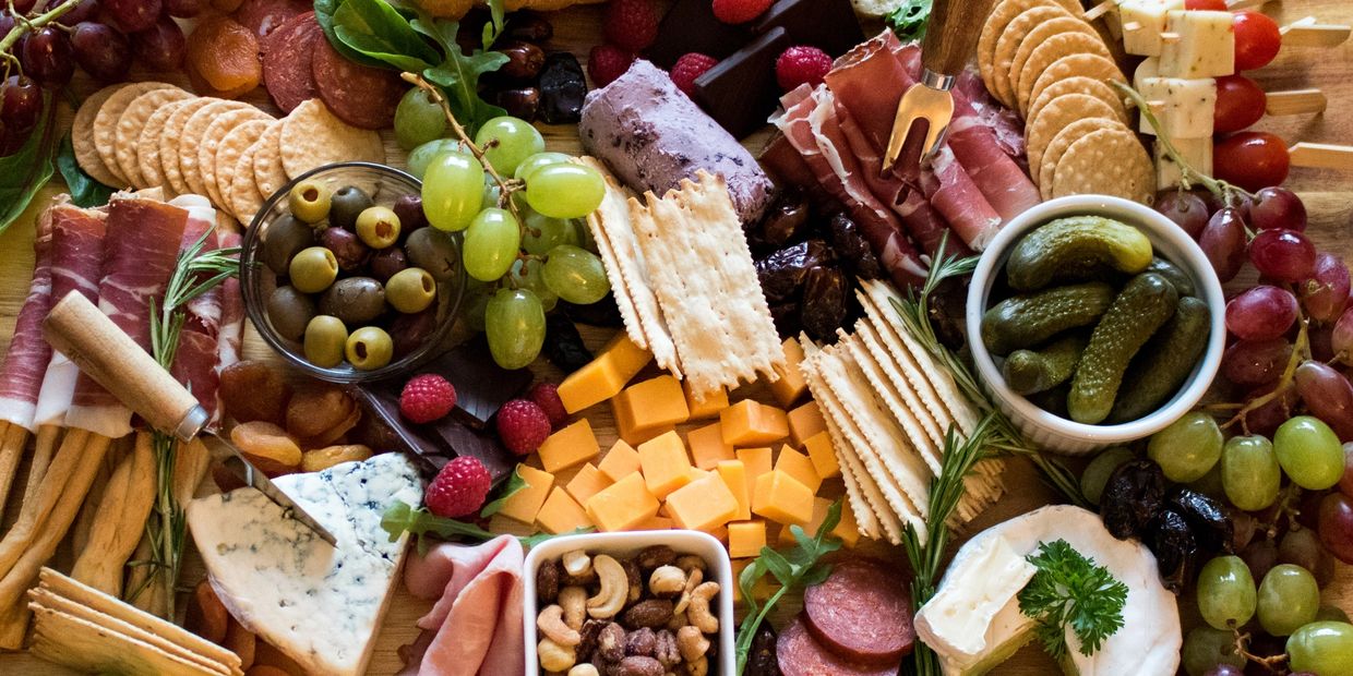 A colorful charcuterie board with cheeses, crackers, meats, fruits, and pickles.