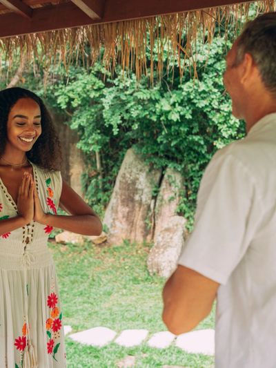 Woman and man greeting each other with Namaste in a tropical outdoor setting.