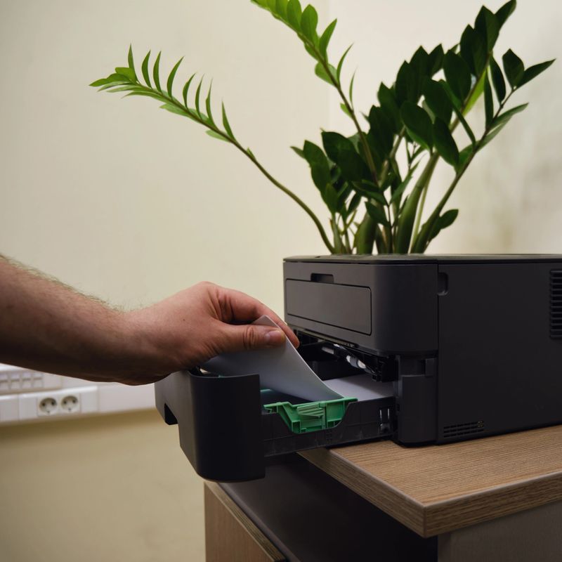 A man hand holds a sheet of paper A4 from a printer in an office room