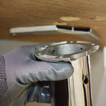 Hand wearing glove holding metal pipe flange under wooden surface.