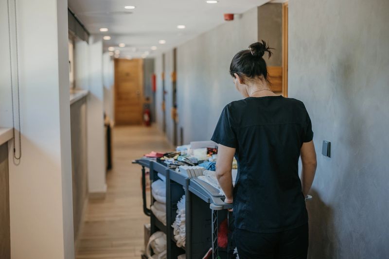 Young hotel maid in uniform pushing chambermaid trolley down the hotel corridor