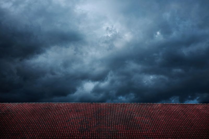Dark Dramatic Sky before Rain and Storm. Cyclone is coming with Black Windy Cloud. House Cover by Red Tiles Roof as foreground. Weather and Season Change