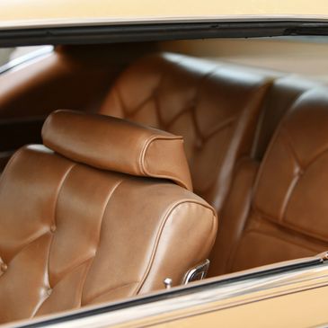 Vintage car interior with tan leather seats and button tufting.