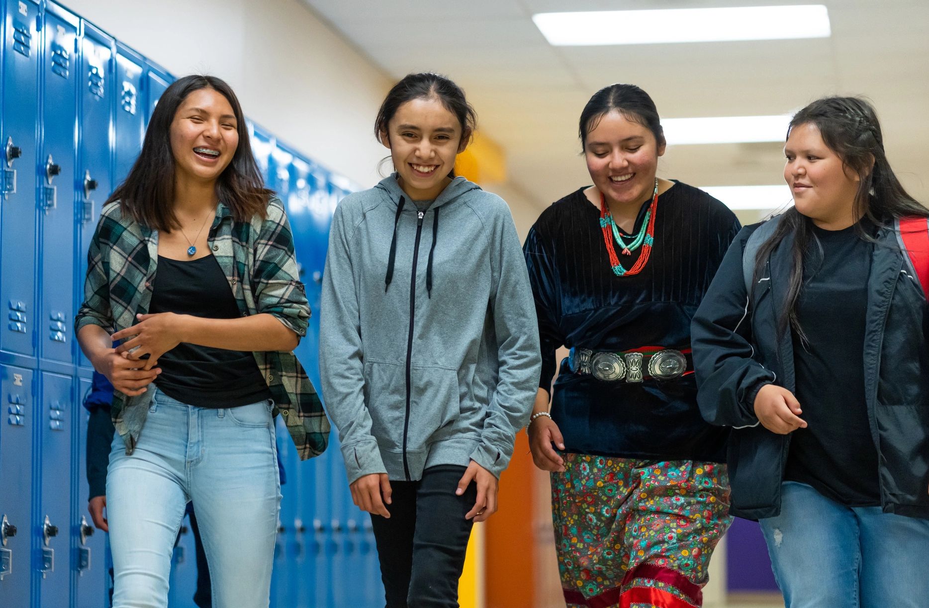 Four girls walking and smiling in a school hallway.