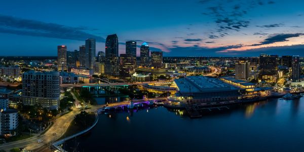 City skyline by the water at dusk with illuminated buildings.