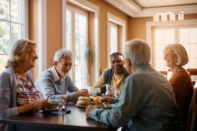 Group of elderly friends enjoying tea and conversation around a table.
