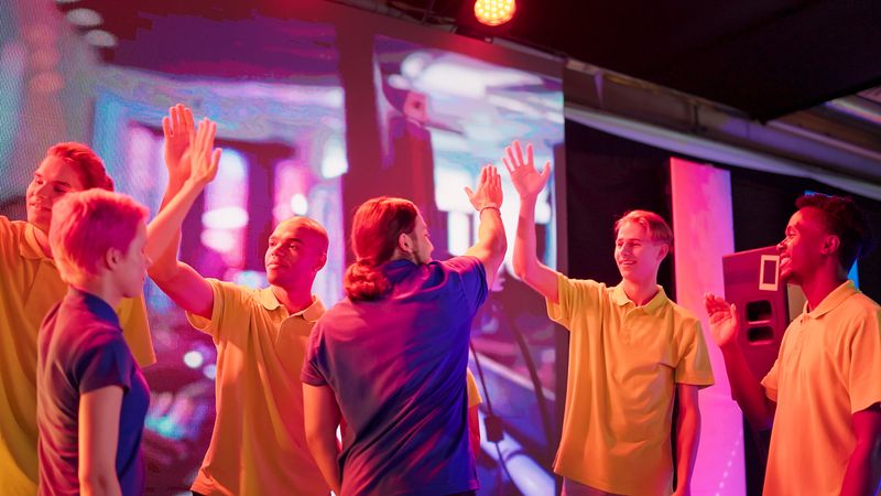 Diverse gamer group wearing yellow t-shirts with african ethnicity players and women on stage receiving a trophy. Doing a group cheer and celebrating victory together.