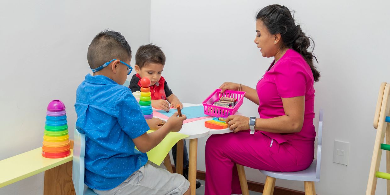 Educadora y niños pintando en una mesa pequeña.