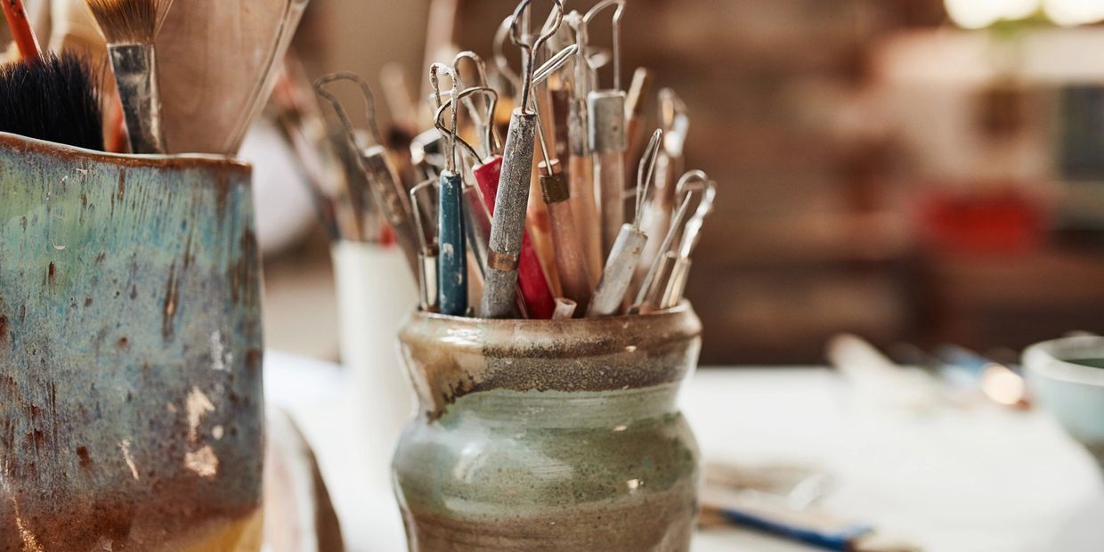 Pottery tools and brushes in ceramic holders on a worktable.