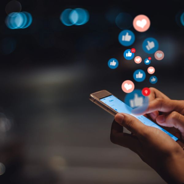 Person using smartphone with social media like and love notifications floating.