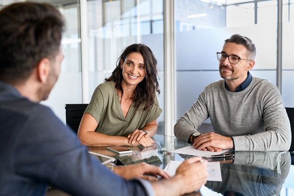 Two professionals smiling during a meeting with a third person.
