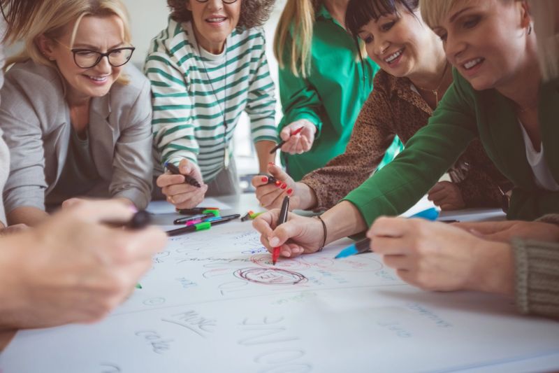 Businesswoman writing on paper while explaining team building concept to colleagues in office