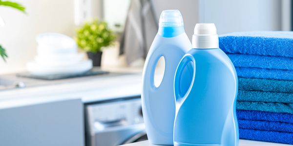 Two blue detergent bottles and neatly folded blue towels in a laundry room.