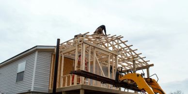 Worker building wooden house frame with machinery assistance.