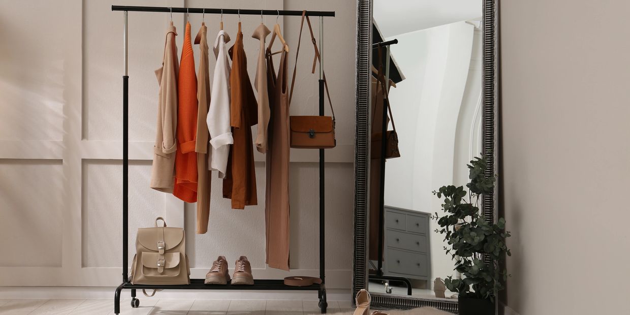 Minimalist clothing rack with neutral-toned outfits and accessories beside a large ornate mirror.