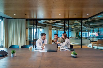 Three colleagues collaborating around a laptop in a modern office.