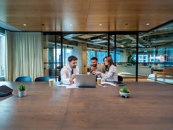 Three colleagues collaborating over a laptop in a modern office conference room.