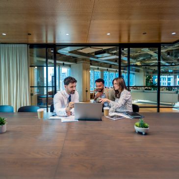 Three coworkers collaborating at a laptop in a modern office.