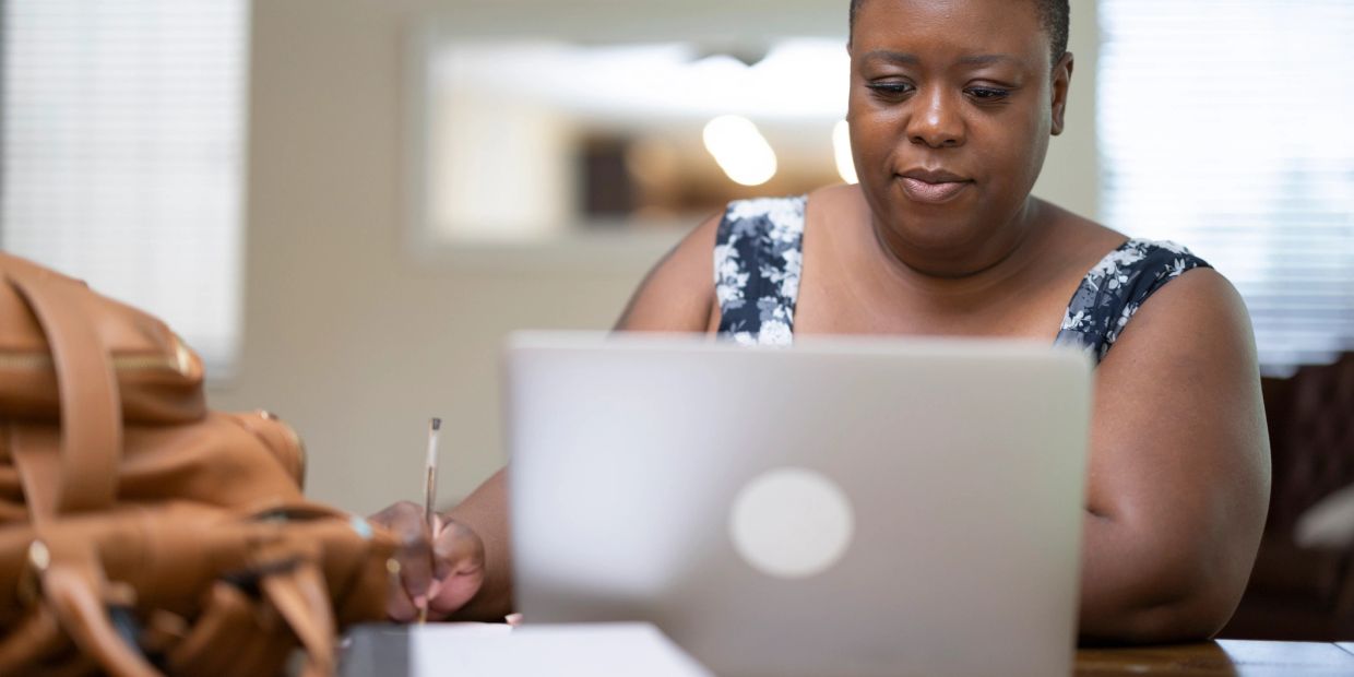 Woman working on laptop and writing notes.