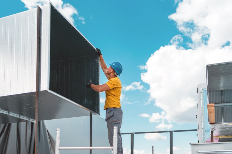 A young Caucasian male construction worker is standing on a construction site and installing an air duct system.