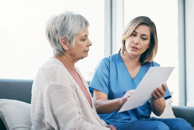 Nurse showing test results to senior woman on paper and talking, discussing and sharing treatment options in old age home. Caregiver, caretaker or medical healthcare professional helping elderly lady