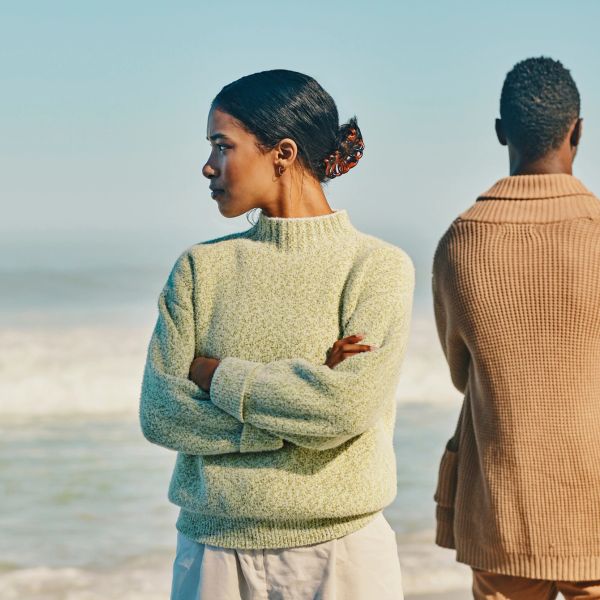 Two people standing apart by the sea, facing opposite directions.
