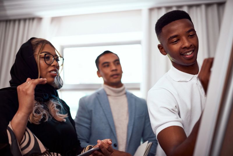 Businesspeople brainstorm and plan a marketing strategy on a whiteboard at work. Diverse and happy team of corporate professionals smiling and discuss while thinking of ideas in the office boardroom